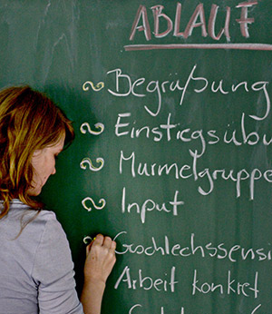 Dozentin schreibt den Ablauf eines Workshops auf eine Tafel.