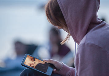 Mädchen mit Kapuze schaut sexuelle Szenen an auf ihrem Handy.